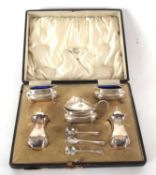 A cased George V silver condiment set comprising two peppers, two open salts, a hinge lidded