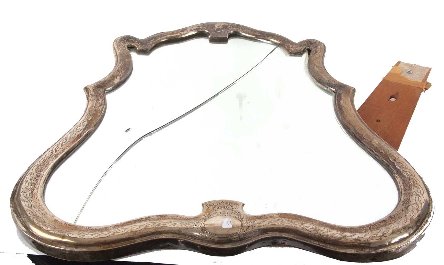 A continental dressing table mirror of escutcheon form, the metal frame engraved with a Celtic