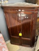 A Georgian mahogany corner cabinet with two panelled doors opening to a painted interior with shaped