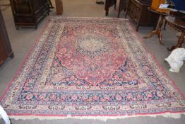 A large Middle Eastern wool floor rug decorated with central floral and geometric panel on a