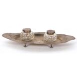 An Edwardian silver ink stand boat shaped and supported on four cast feet, the centre with two cut