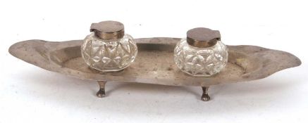 An Edwardian silver ink stand boat shaped and supported on four cast feet, the centre with two cut
