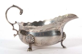 A George VI silver sauce boat of typical form with card cut rim and flying leaf cap handle,