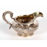 A William IV silver cream jug of compressed circular form, elaborately embossed, chased and engraved