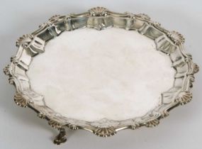 A George III silver waiter or small salver having a pie crust rim with shell motifs, supported on