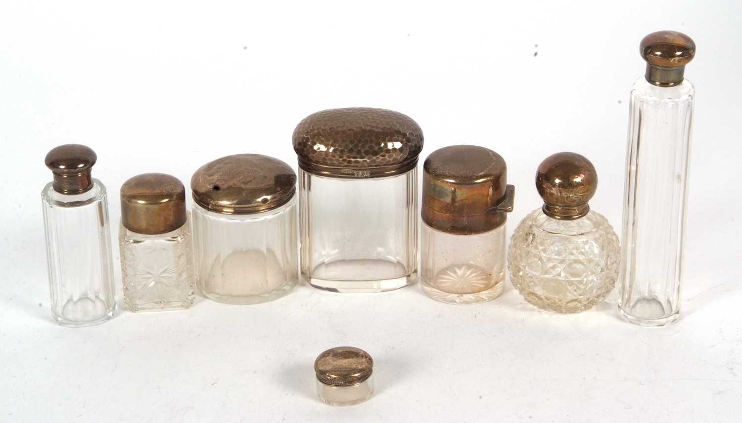 Group of eight glass dressing table jars with hallmarked silver lids, various dates and makers