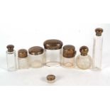 Group of eight glass dressing table jars with hallmarked silver lids, various dates and makers