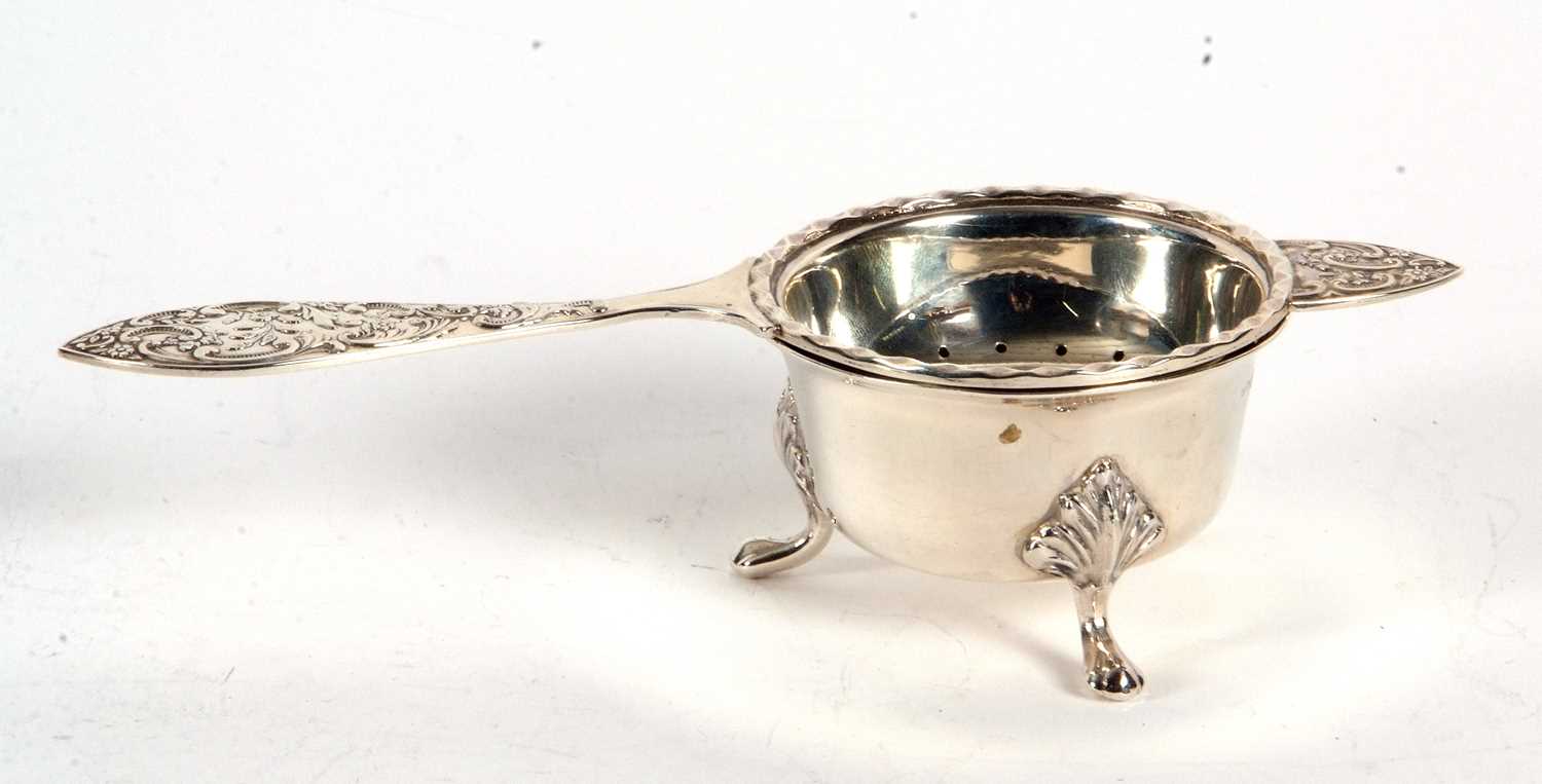 A hallmarked silver tea strainer and bowl, the tea strainer with pierced bowl and applied wavey