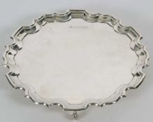 A sterling silver card salver of plain form, having pie crust edge and supported on three cast