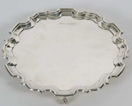 A sterling silver card salver of plain form, having pie crust edge and supported on three cast