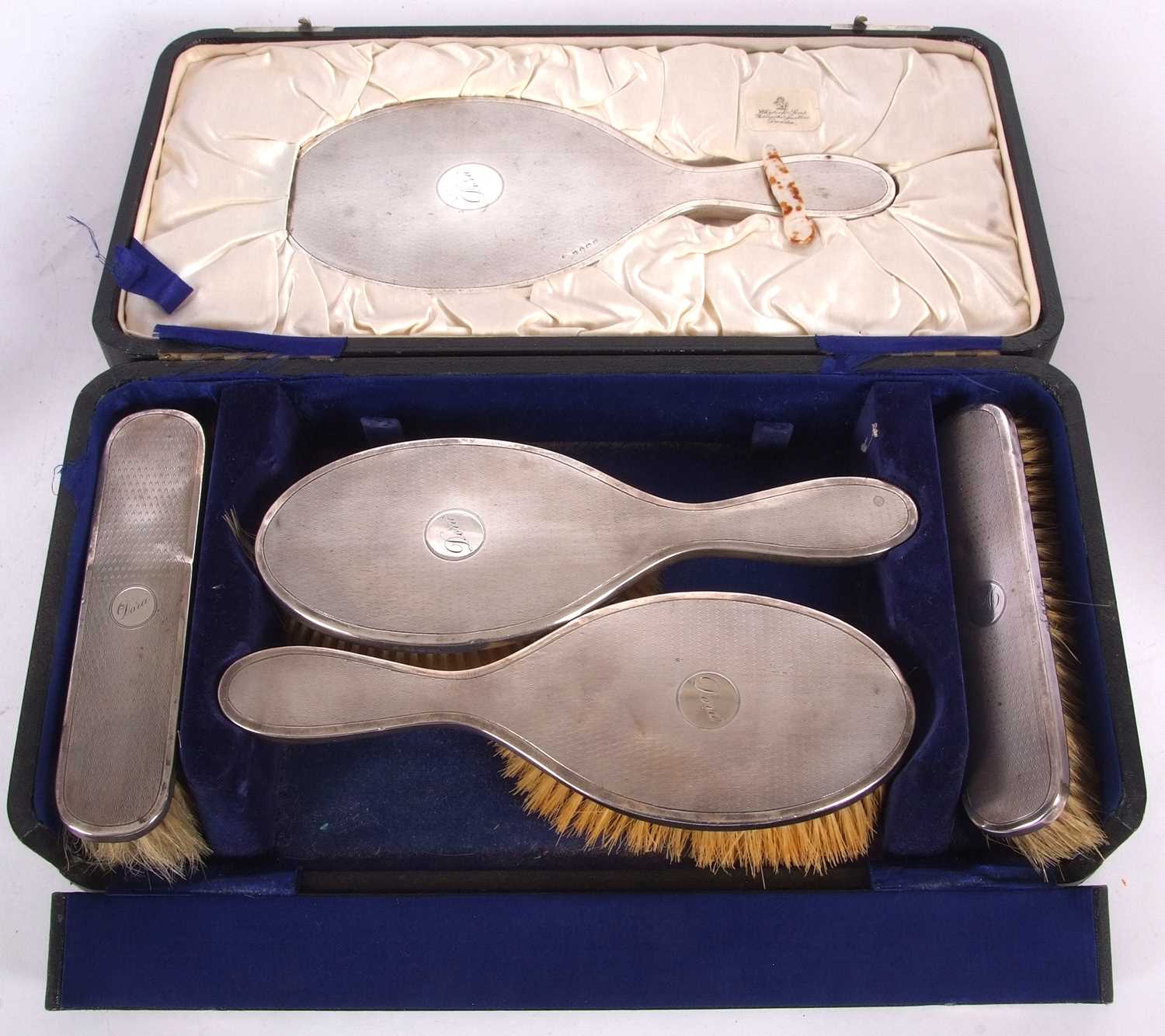 A cased George V silver backed dressing table set comprising hand mirror, two clothes brushes, two