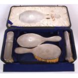 A cased George V silver backed dressing table set comprising hand mirror, two clothes brushes, two