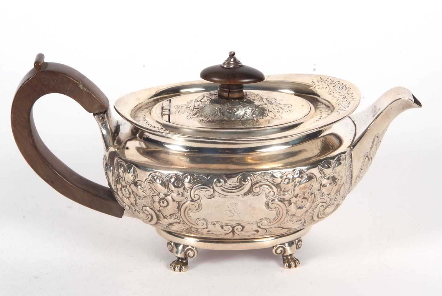 A George III silver teapot of oval form and elaborately decorated with scrolled flowers,