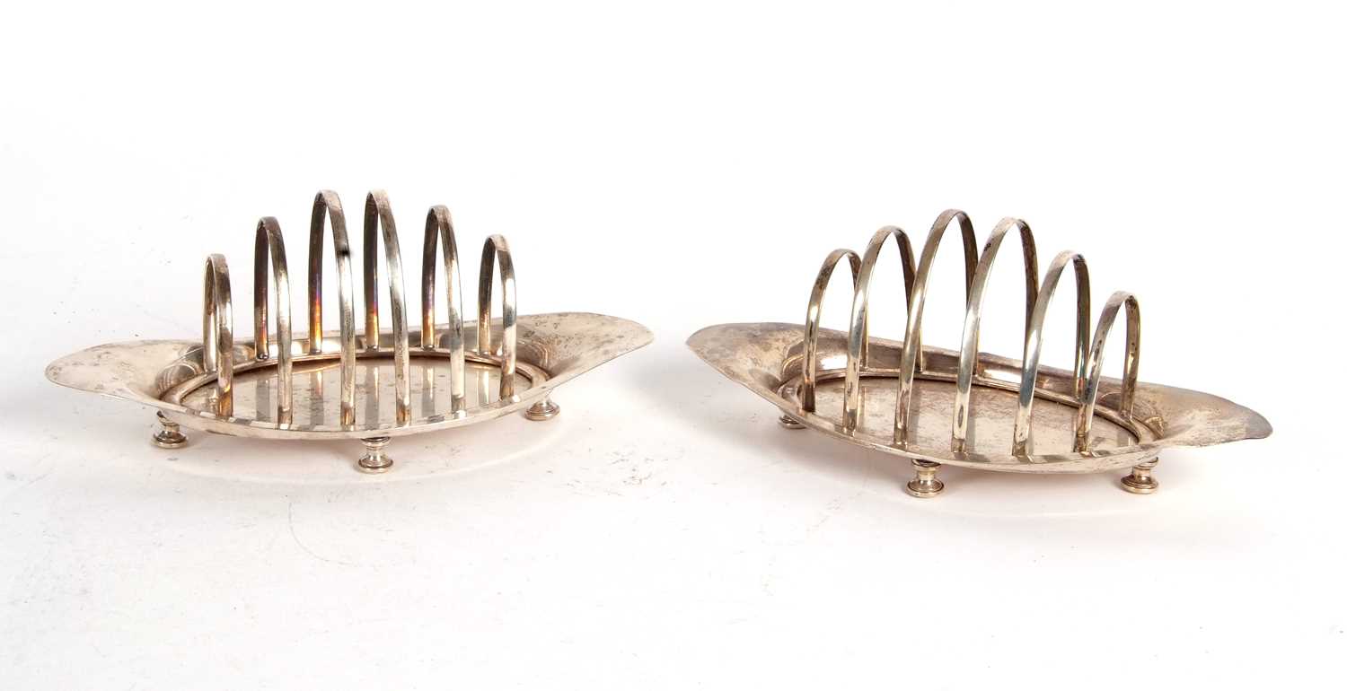 A pair of Edwardian silver toast racks, boat shaped, each with six graduated dividers, supported
