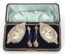 A cased late Victorian pair of boat shaped pedestal salts, floral scroll embossed together with