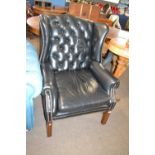 A black buttoned leather upholstered wing chair with hardwood legs orginally purchased from Harrods,