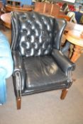 A black buttoned leather upholstered wing chair with hardwood legs orginally purchased from Harrods,