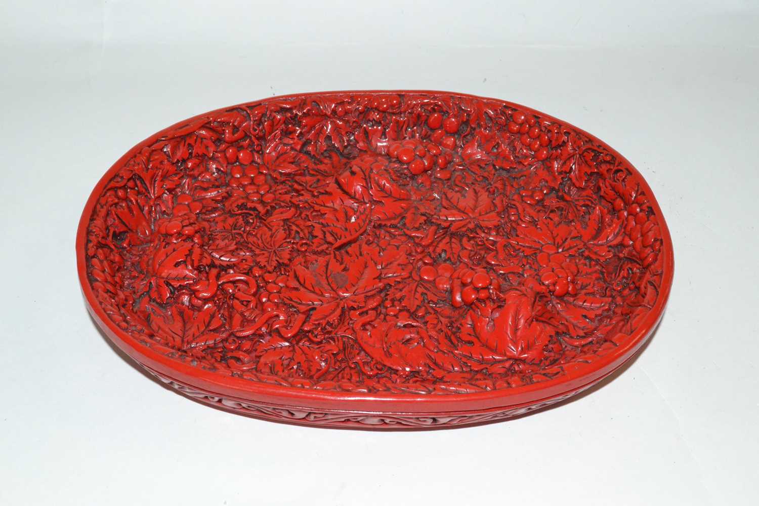 A Chinese red lacquer dish with raised relief decoration of berries and leaves, seal mark to base,