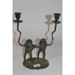 A metal candle holder shaped as two frogs, each holding a candle sconce on oval metal base