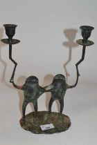 A metal candle holder shaped as two frogs, each holding a candle sconce on oval metal base