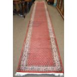 An Iranian wool runner carpet decorated with a large repetitive central panel with leaf decoration