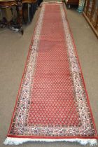 An Iranian wool runner carpet decorated with a large repetitive central panel with leaf decoration