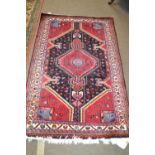 A modern Persian wool rug decorated with large central geometric panel on a red and blue background,