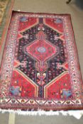 A modern Persian wool rug decorated with large central geometric panel on a red and blue background,