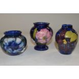 A group of three small Moorcroft vases, all with hibiscus or anemone designs on a blue ground