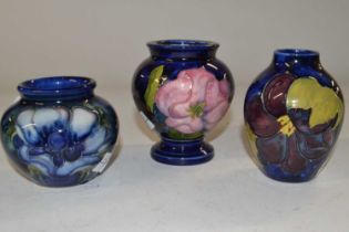 A group of three small Moorcroft vases, all with hibiscus or anemone designs on a blue ground