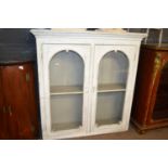 A cream painted Victorian glazed cupboard with two arched doors and shelved interior, 138cm wide