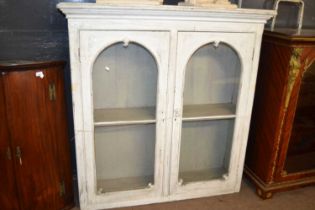 A cream painted Victorian glazed cupboard with two arched doors and shelved interior, 138cm wide