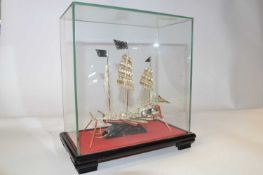 A white metal model of a Chinese junk, in glass case