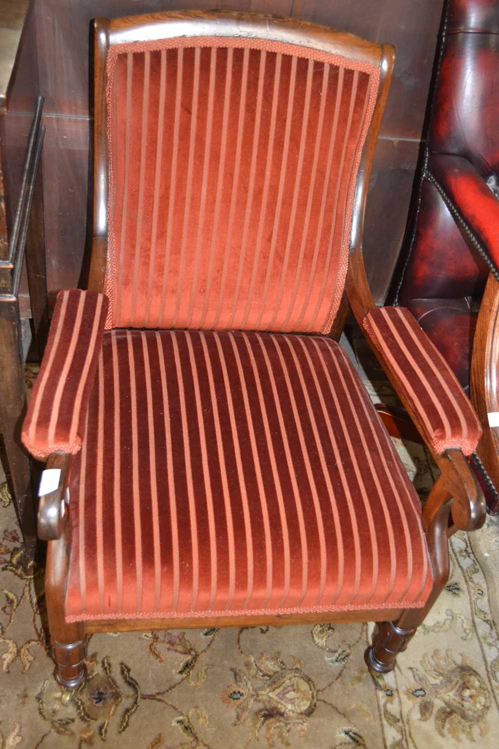 A Victorian rosewood framed and striped upholstered armchair with turned legs and casters