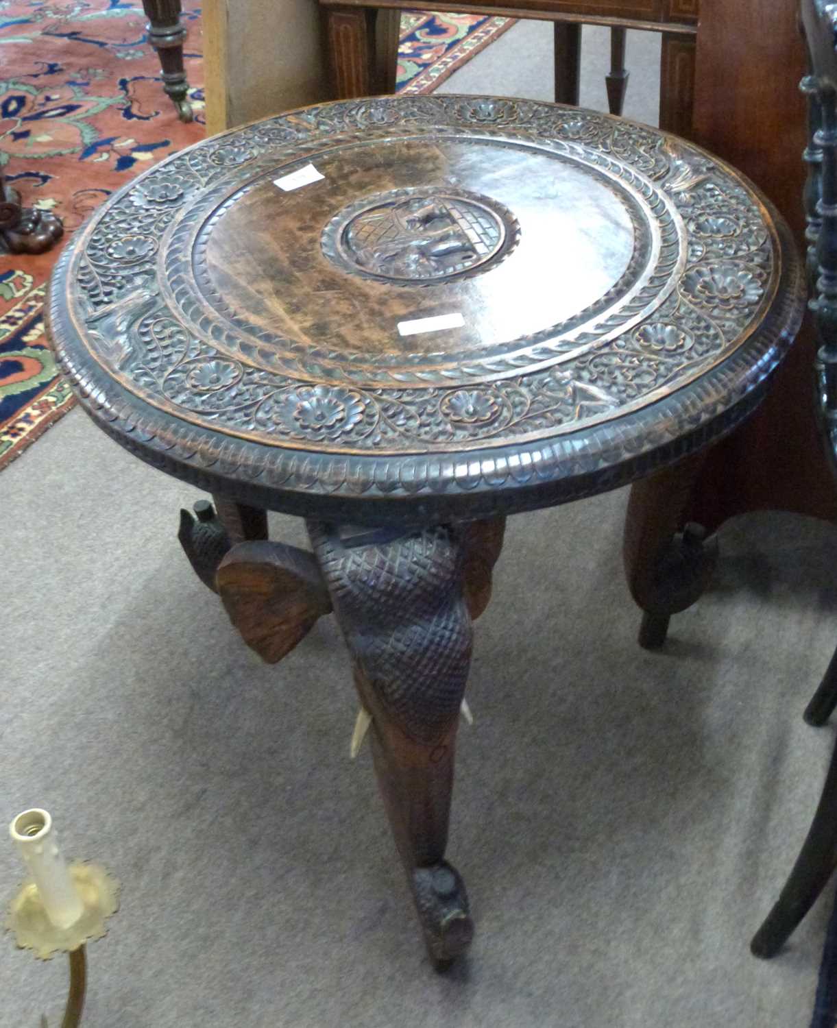 An Indian hardwood occasional table with circular carved top supported on elephant shaped legs,