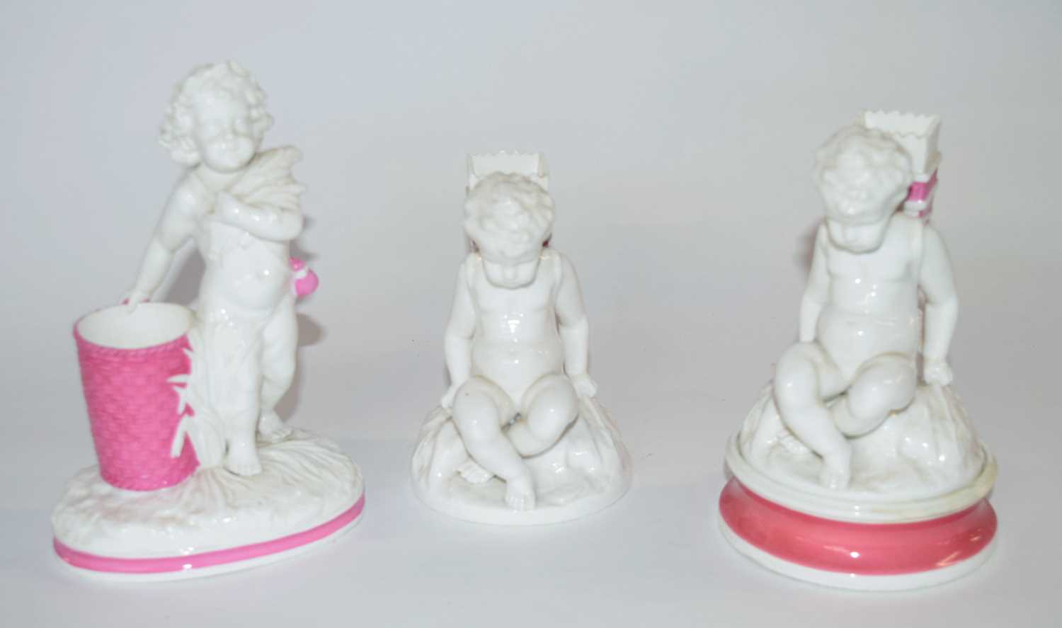 A group of three 19th Century white glazed spill vases, modelled as cherubs, one on a pink