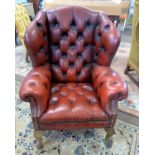 A distressed red leather Chesterfield style wing back armchair Back leg damaged and repaired with