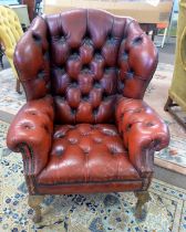 A distressed red leather Chesterfield style wing back armchair Back leg damaged and repaired with