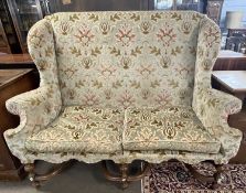 A Carolean style wing back sofa with floral upholstery and turned legs united by two X formed