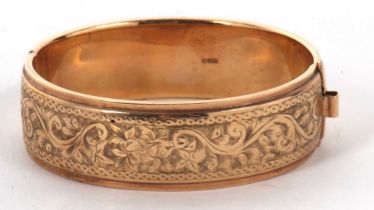 A 9ct gold bangle, the upper half with engraved decoration with plain lower half, 19mm wide,