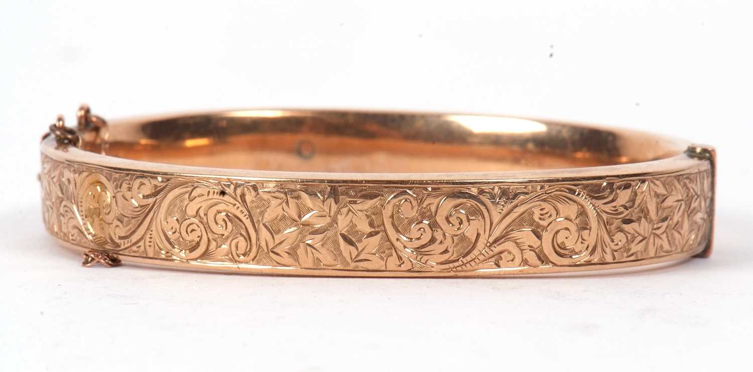A 9ct hinged bangle, the 9mm wide bangle with engraved decoration to upper half and plain lower