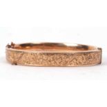 A 9ct hinged bangle, the 9mm wide bangle with engraved decoration to upper half and plain lower