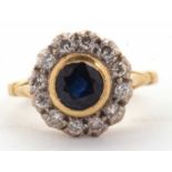 An 18ct sapphire and diamond ring, the central round sapphire in a rubover mount, surrounded by