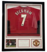 A Manchester United football shirt, bearing the signature of David Beckham in black ink. Framed
