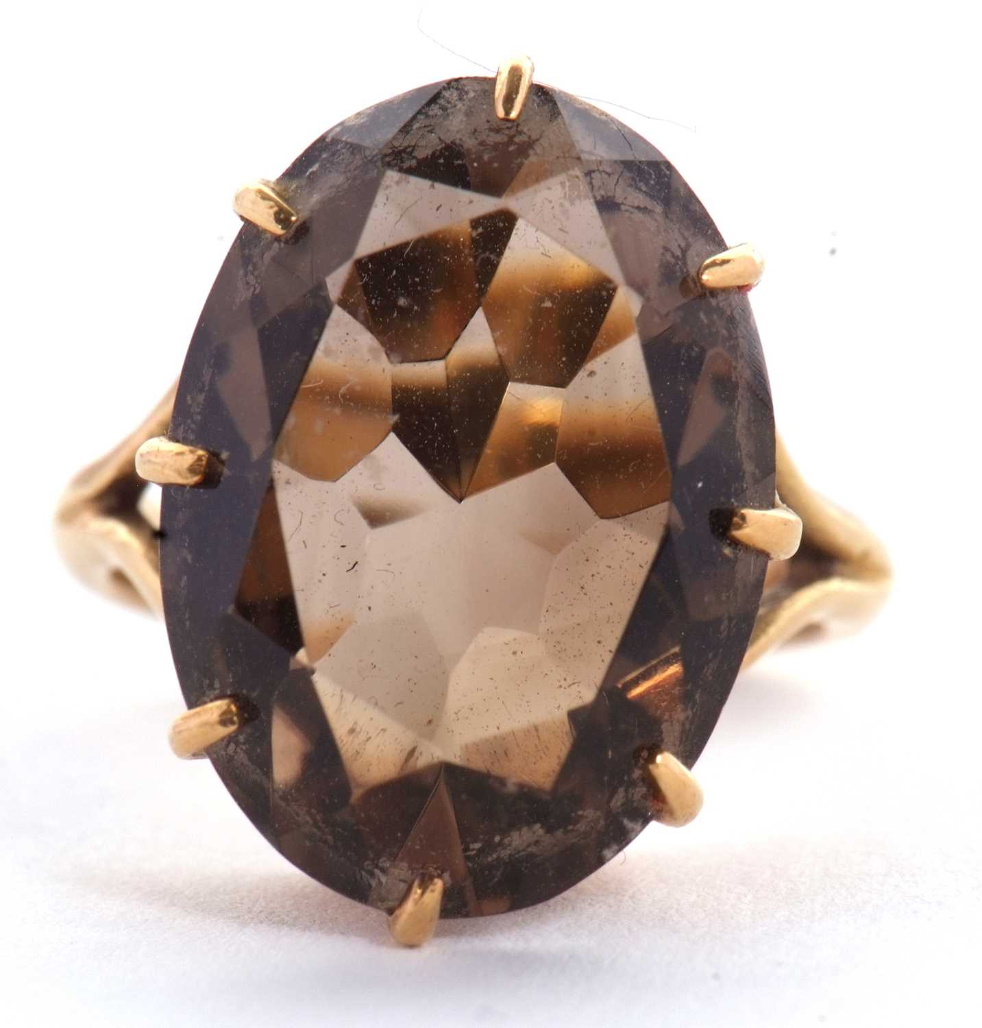 A smokey quartz ring, the oval mixed cut smokey quartz, claw mounted with split shoulders and