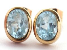 A pair of blue topaz earrings, the oval mixed cut blue topaz in rubover mounts of yellow metal