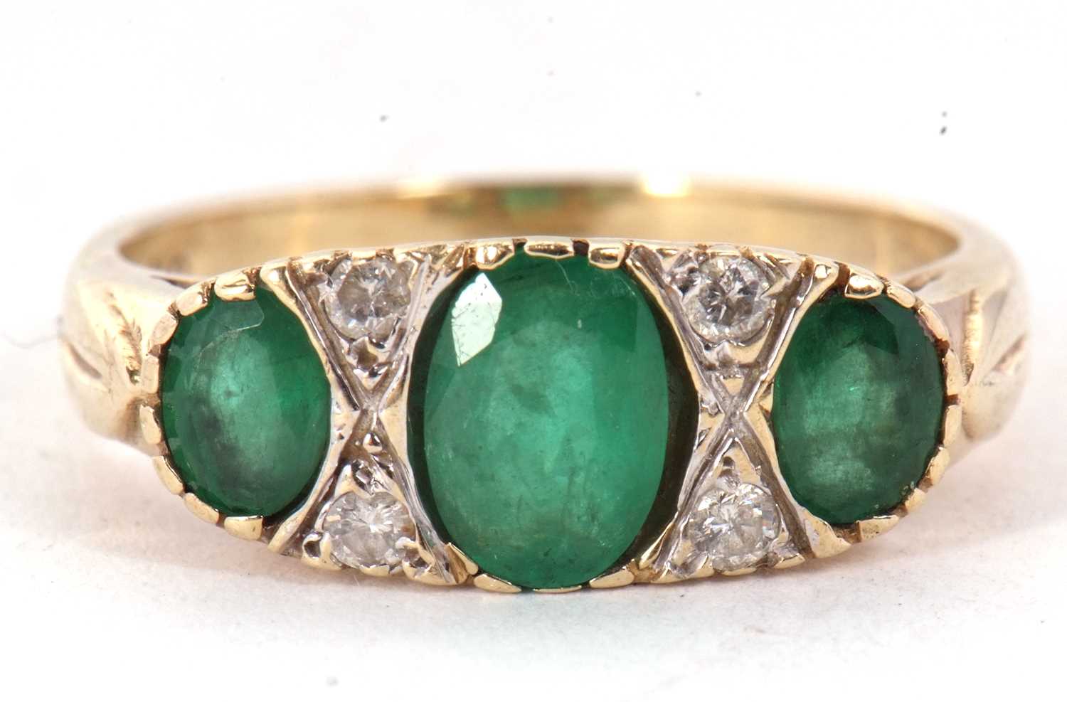 A 9ct emerald and diamond ring, the three graduated oval emeralds, interspaced with two small