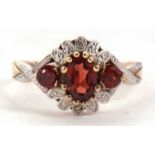A 9ct garnet and diamond ring, set with a central round garnet with an oval garnet to either side,