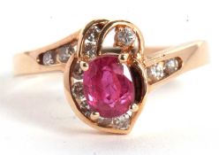 A 14k ruby and diamond ring, the central four claw mounted oval ruby, asymetrically set with small