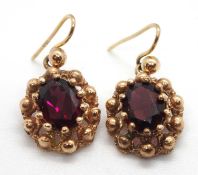 A pair of garnet earrings, the oval claw mounted garnets in a beaded surround, all set in unmarked